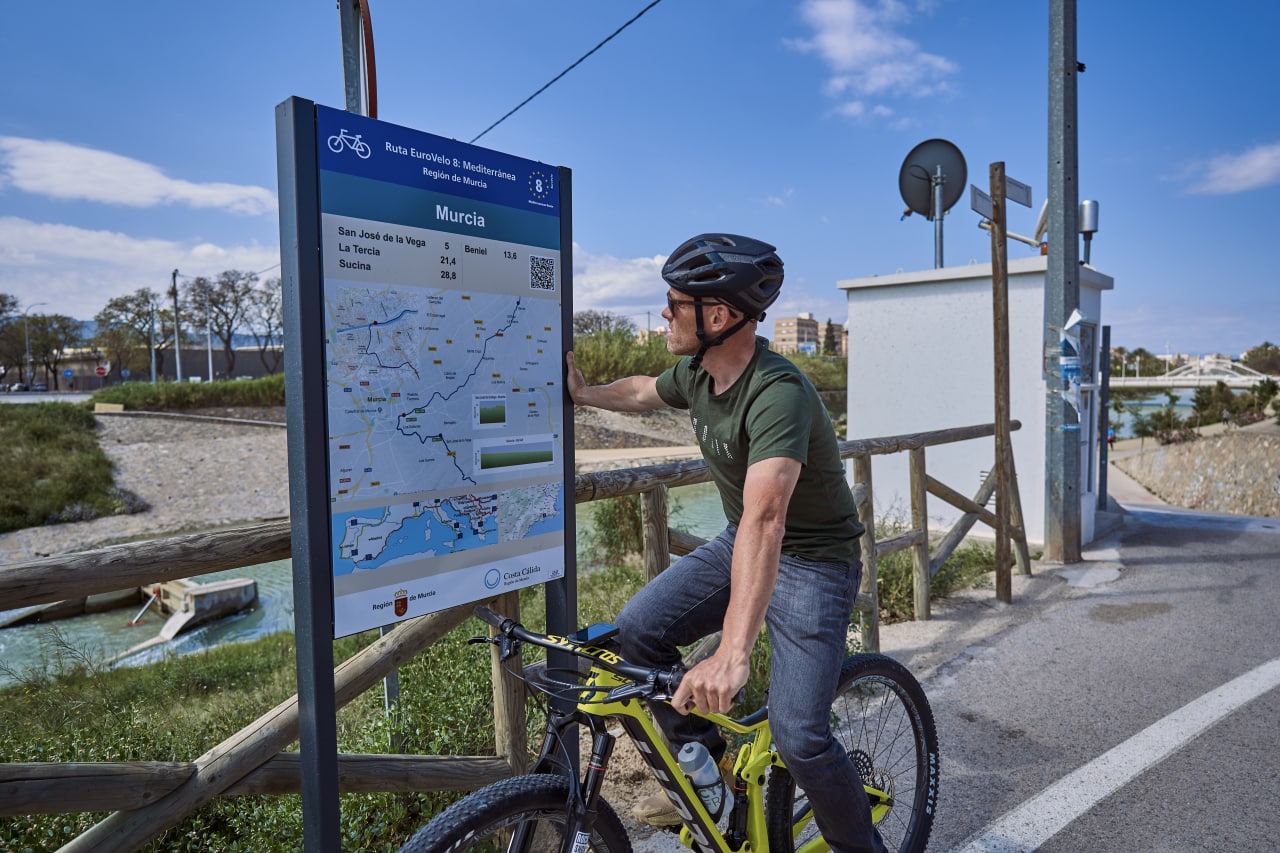 Un ciclista consulta en un poste informativo el itinerario de la Red Eurovelo en la Región