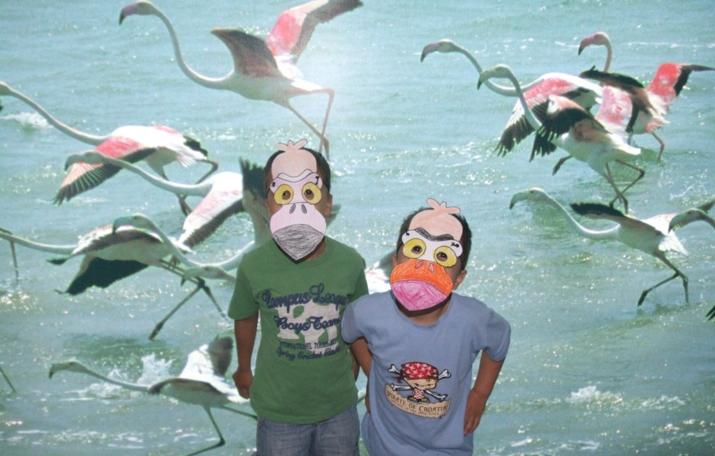 La imagen muestra a dos niños participantes en un taller de confección de máscaras con la imagen de los flamencos del parque Salinas y Arenales de San Pedro del Pinatar.