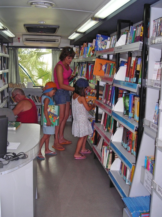 Varios veraneantes escogen libros en un 'Bibliobús' de la Biblioteca Regional